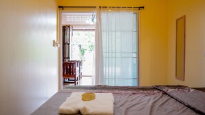 A bedroom with a bed, a window with curtains, and a view of an outdoor area with a chair and table. - Chan De Bua (Chanthaburi)