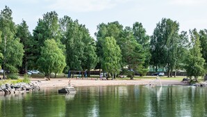 A park with a playground, a sandy area, and a calm lake. - First Camp Ekudden Mariestad (Mariestad)