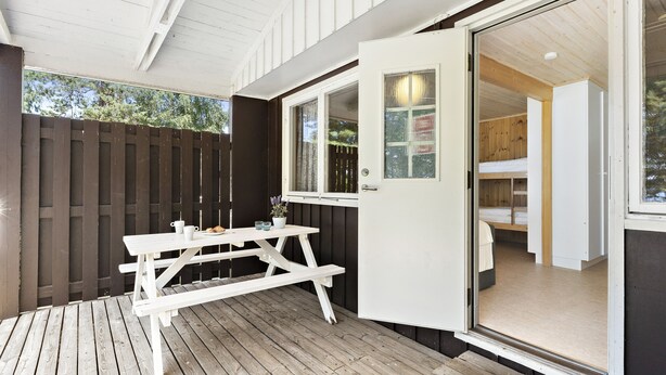 A wooden deck with a picnic table, a sliding glass door leading to a bedroom with a bed and a wardrobe. - First Camp Ekudden Mariestad (Mariestad)