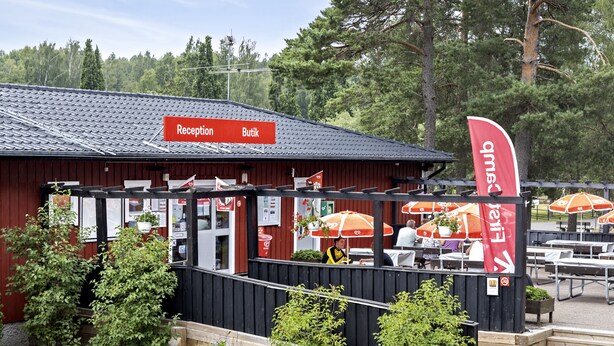 A restaurant with outdoor seating, a red sign indicating the reception and buffet area, and a flag with the restaurant's logo. - First Camp Hökensås Tidaholm (Tidaholm)