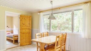 A room with a wooden dining table, chairs, a window with a view of trees, and a door leading to another room. - First Camp Hökensås Tidaholm (Tidaholm)