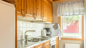 A kitchen with wooden cabinets, a stainless steel sink, a stove, and a window with a plaid valance. - First Camp Hökensås Tidaholm (Tidaholm)