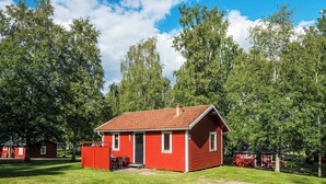 A red wooden cabin with a tiled roof, surrounded by a grassy area and trees. - First Camp Hökensås Tidaholm (Tidaholm)