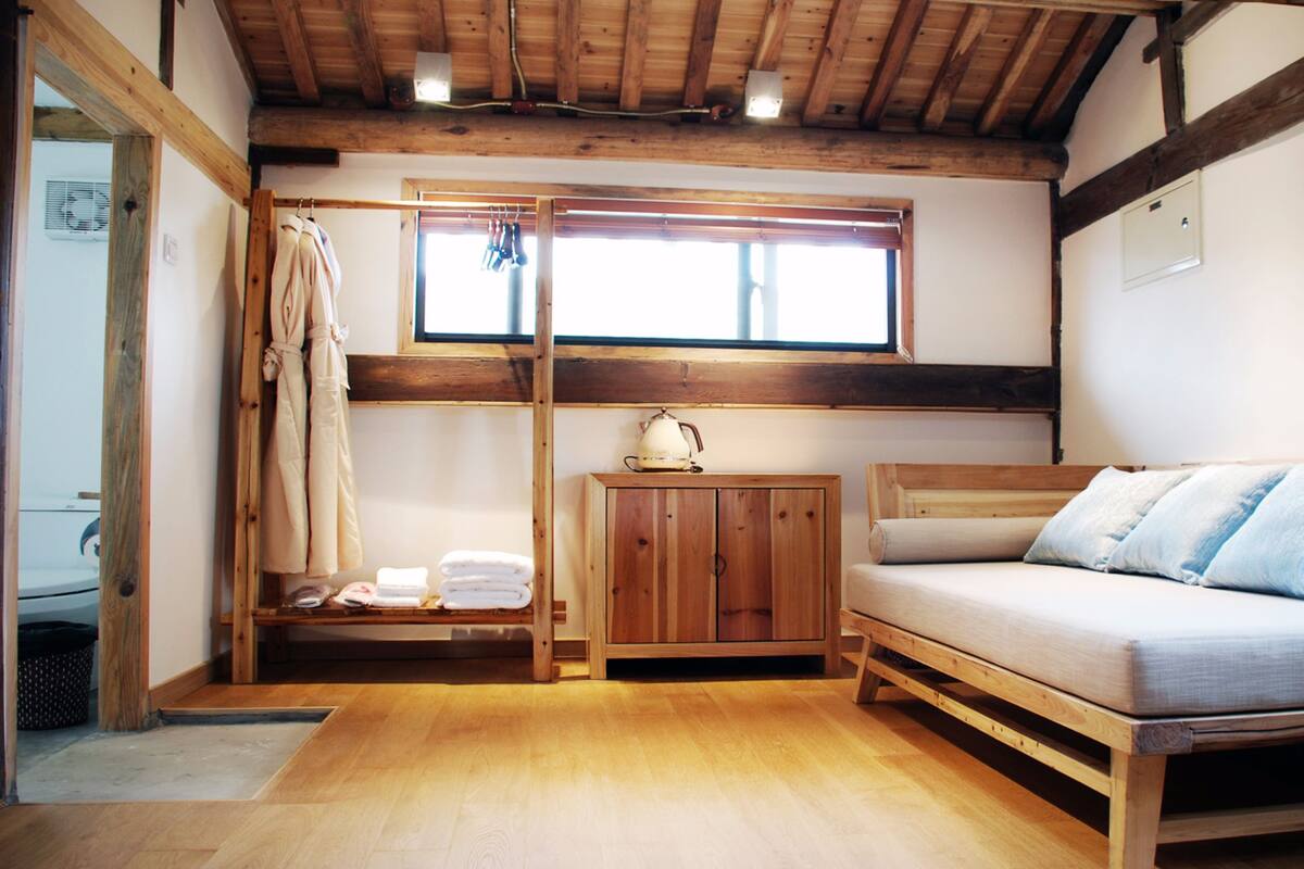 Una habitación acogedora con una cama de madera, un pequeño armario de madera y un ventanal con cortinas.