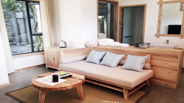 A modern room with a wooden sofa, a small wooden table with a remote control and a mug, a wooden cabinet, a wooden bench, a wooden bench with a white towel, a wooden bench with a white towel, a wooden bench with a white towel, a wooden bench with a white towel, a wooden bench with a white towel, a wooden bench with a white towel, a wooden bench with a white towel, a wooden bench with a white towel, a wooden bench with a white towel, a wooden bench with a white towel, a wooden bench with a white towel, a wooden bench with a white towel, a wooden bench with a white towel, a wooden bench with a white towel, a wooden bench with a white towel, a wooden bench with a white towel, a wooden bench with a white towel, a wooden bench with a white towel, a wooden bench with a white towel, a wooden bench with a white towel, a wooden bench with a white towel, a