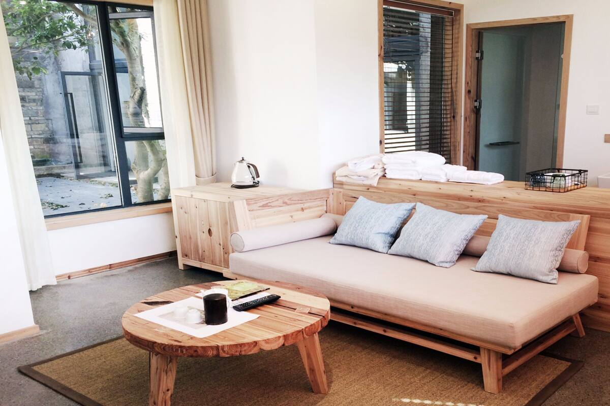 Una habitación moderna con un sofá de madera, una mesita de madera con un control remoto y una taza, un armario de madera, un banco de madera, un banco de madera con una toalla blanca, repetido 23 veces.