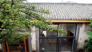 A traditional building with a tiled roof, a glass door, and a visible interior with a table and chairs.