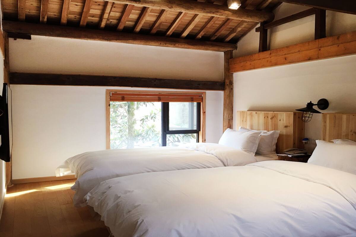Un dormitorio con dos camas, vigas de madera, un ventanal y una mesita de noche.