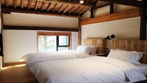 A bedroom with two beds, wooden beams, a window, and a nightstand.