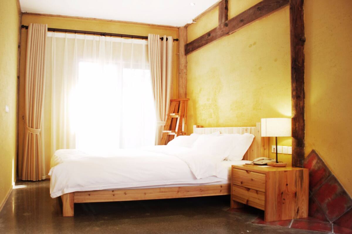 Una cama de madera en una habitación con paredes amarillas, una escalera de madera, una mesita de noche con una lámpara y un teléfono.