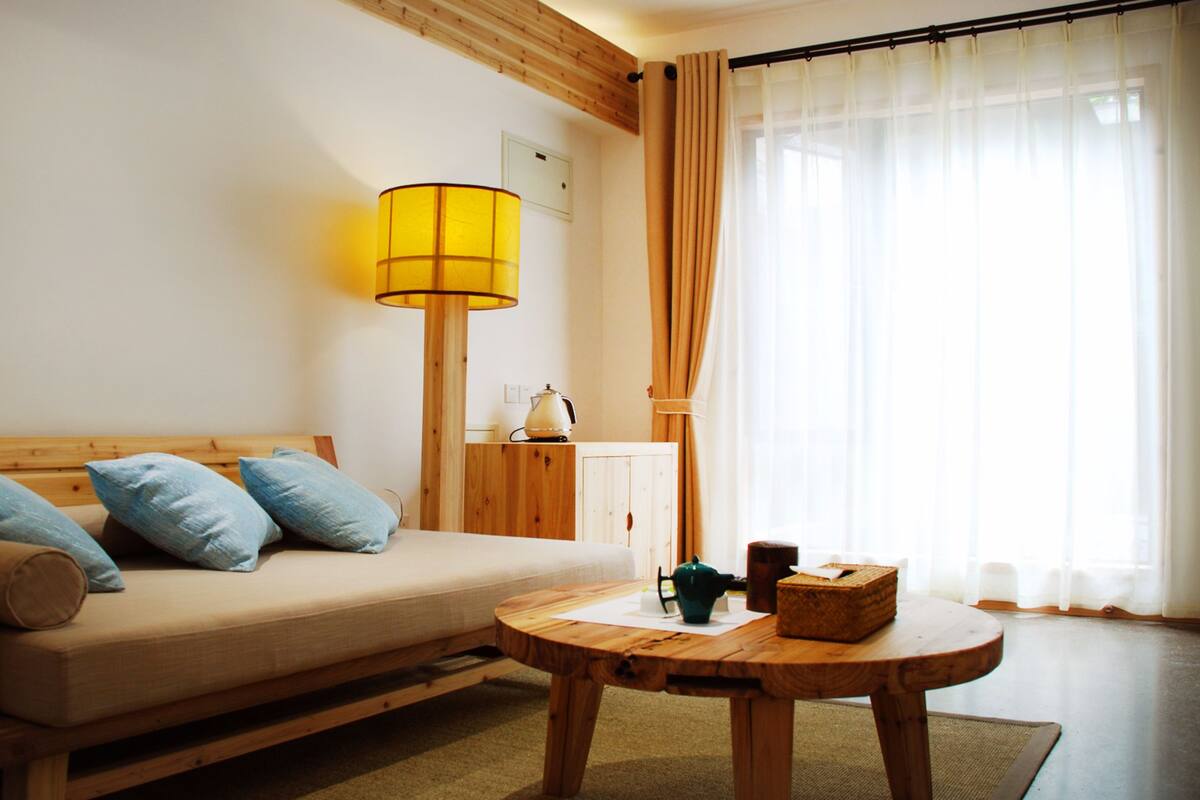 Una habitación acogedora con un sofá de madera, una mesa de centro de madera, una lámpara y una ventana con cortinas.