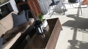 A sunlit patio with a wicker sofa, a metal chair, and a small table with a potted plant. - Bryne Hotell (Time)
