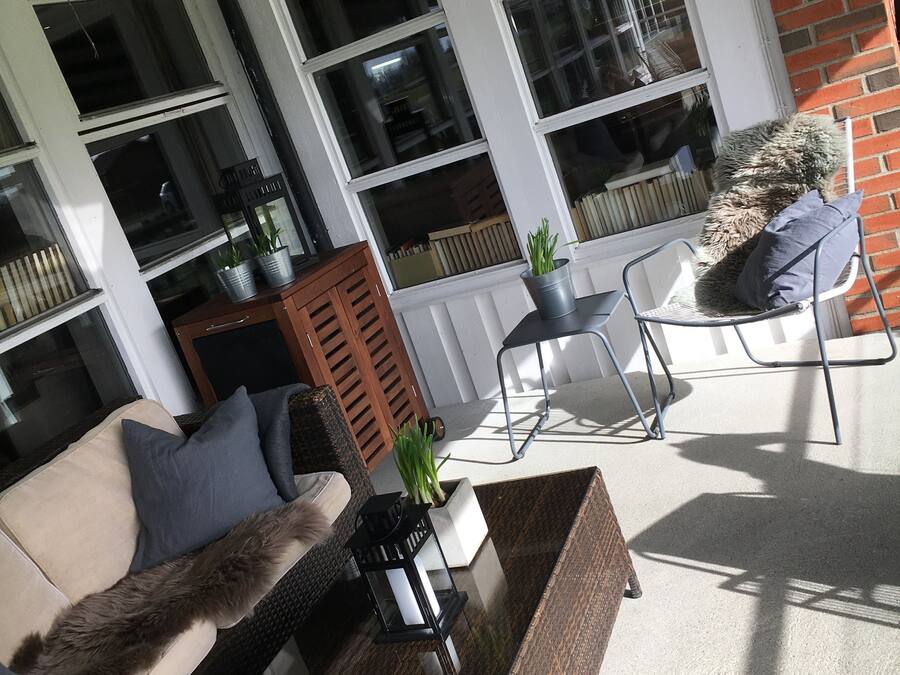 A sunlit patio with a wicker sofa, a metal chair, and a small table with a potted plant.