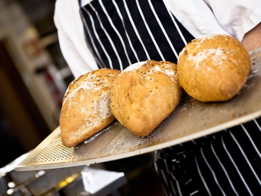 A person holding a tray with three loaves of bread.