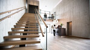 A modern interior with a wooden staircase, a reception desk, and a high ceiling. - Bryne Hotell (Time)
