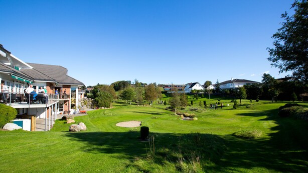 A golf course with a clubhouse, a well-maintained lawn, and several buildings in the background. - Bryne Hotell (Time)