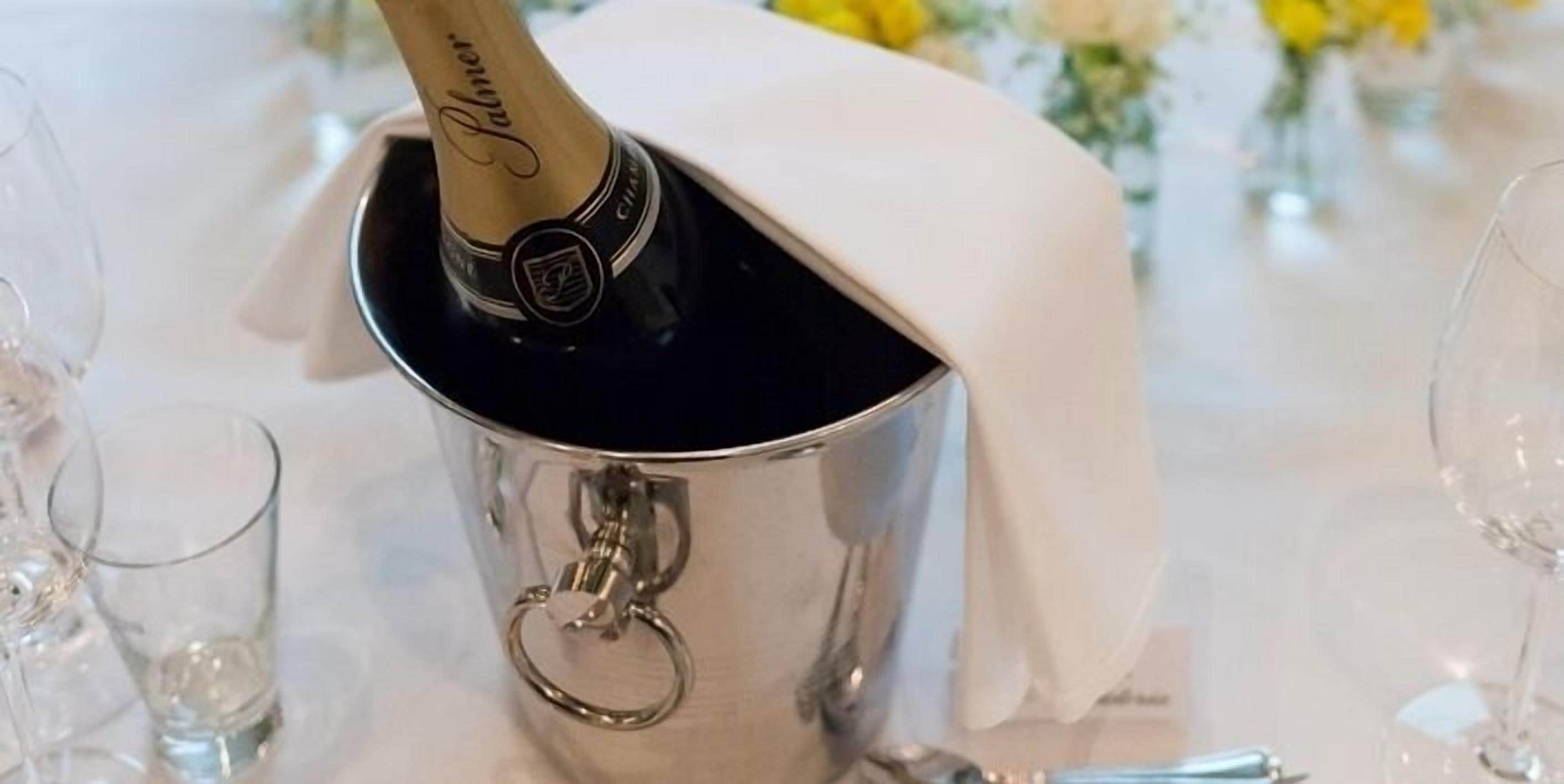 A champagne bottle in a silver bucket with a keychain attached, placed on a table with a white cloth.