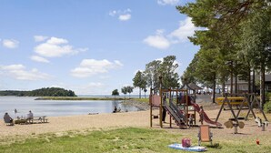 A lakeside park with a playground, picnic tables, and a sandy beach. - First Camp Mörudden Karlstad (Hammaro)