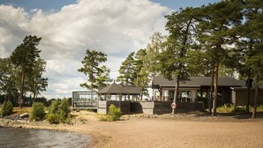 A beachside property with a wooden cabin, a glass-roofed structure, and a large tree. - First Camp Mörudden Karlstad (Hammaro)