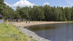 A lakeside area with a sandy beach, a small dock, and a playground. - First Camp Mörudden Karlstad (Hammaro)