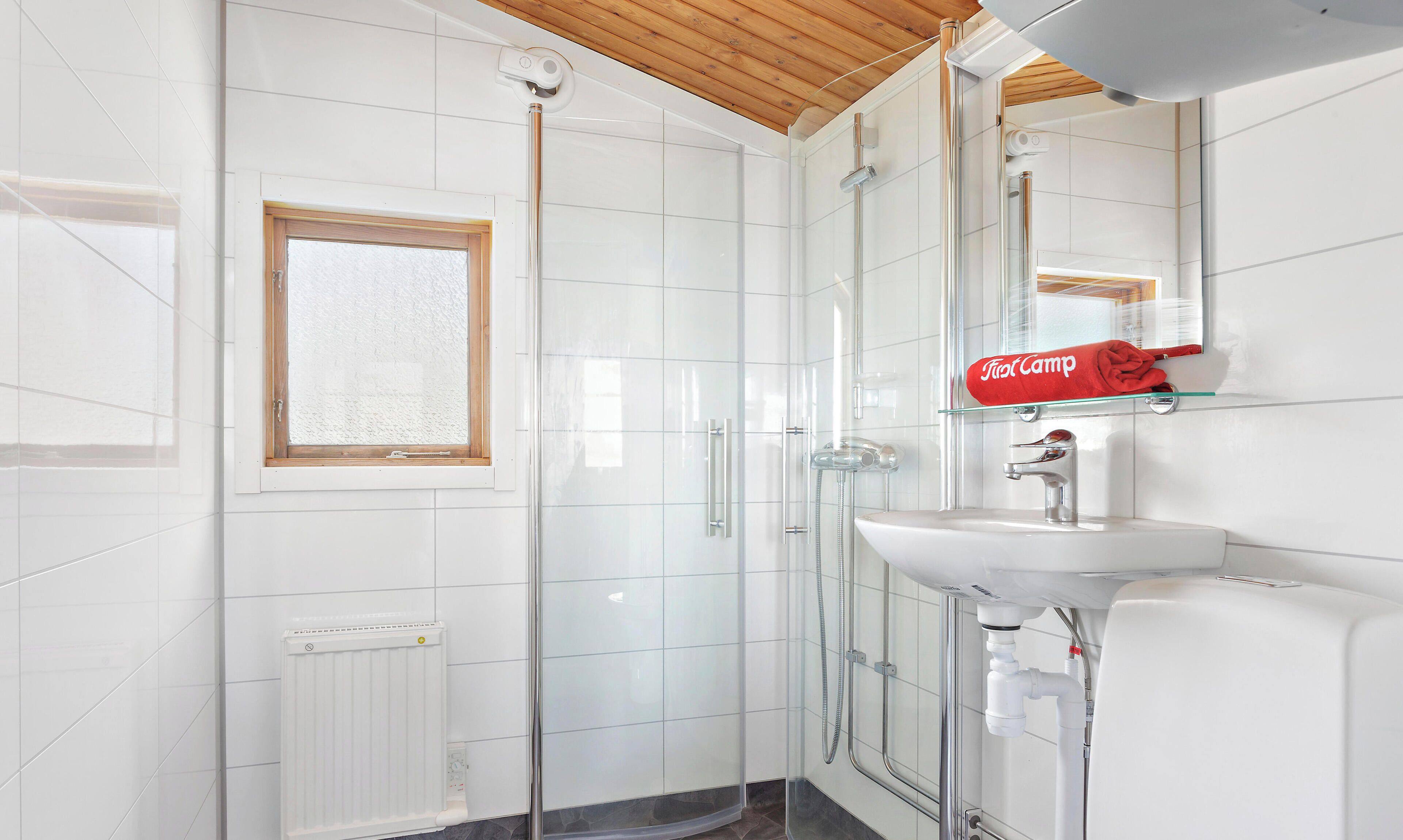 A modern bathroom with a glass shower enclosure, a white sink, and a towel rack with a red towel.