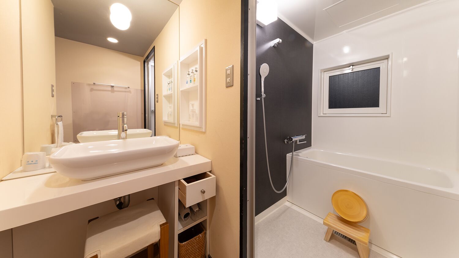 A bathroom with a white sink, mirror, shower, and a small wooden stool.