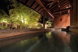 A serene indoor pool area with wooden beams and a calm water surface, surrounded by lush greenery. - Hagihonjin (Hagi)