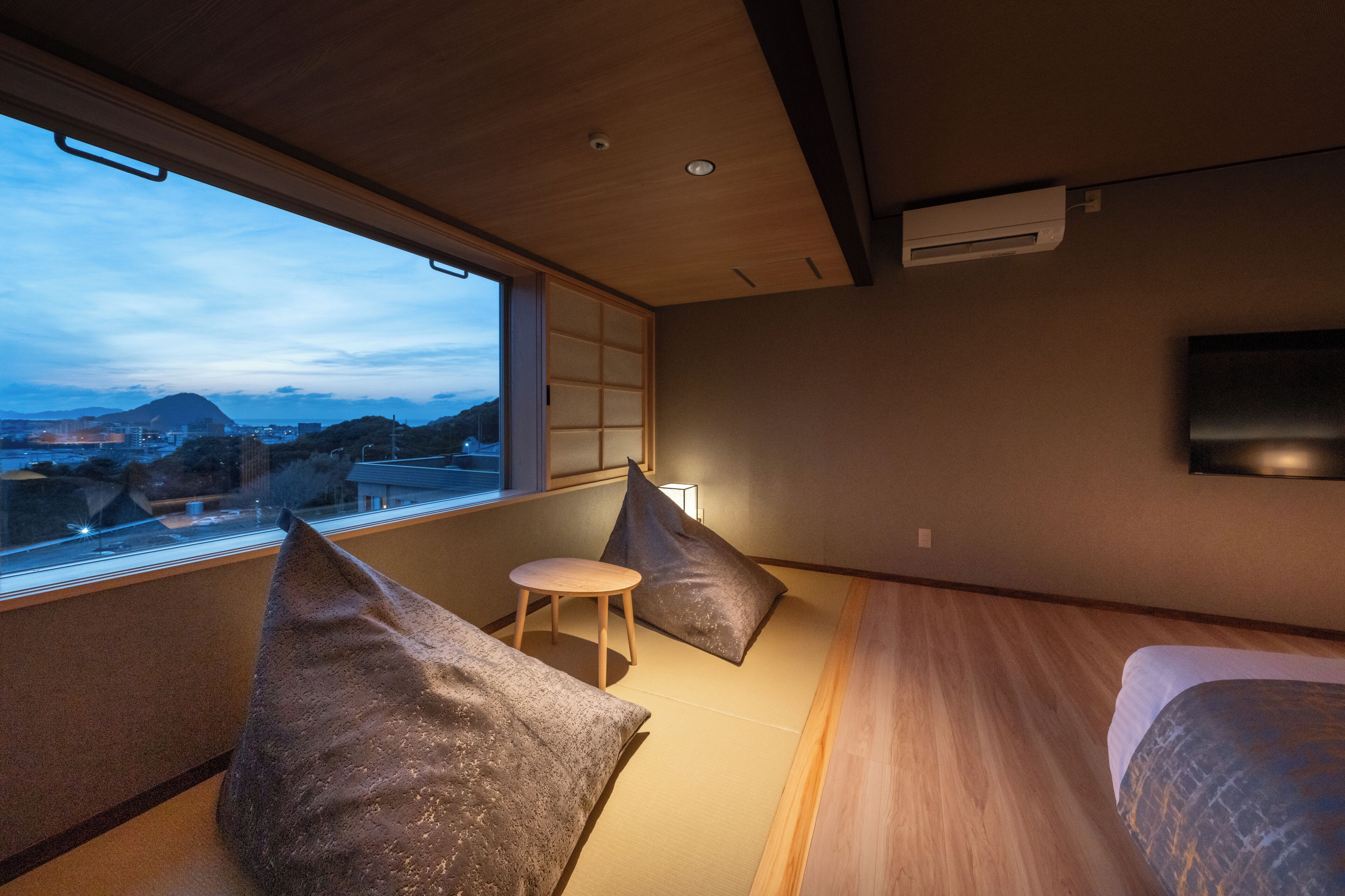 A modern room with a large window, a bed, a small table, and a wall-mounted TV.