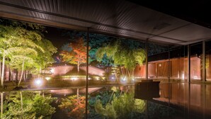 Un edificio moderno con grandes ventanales que reflejan un jardín con árboles y un estanque.