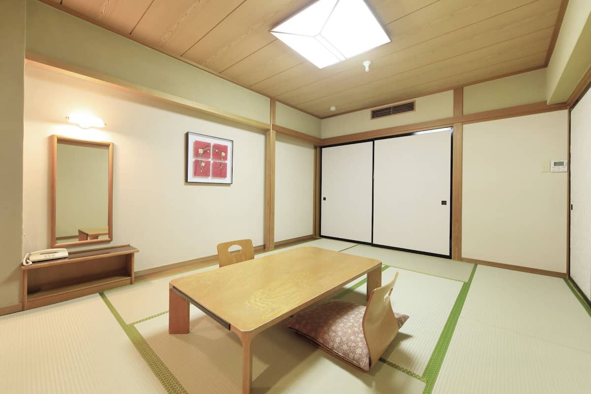Una habitación japonesa tradicional con suelo de tatami, una mesa baja, una silla, un espejo y puertas correderas.