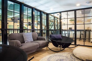 A modern interior with a sofa, a black chair, and a large window. - Travel Light Hostel Pattaya (Pattaya)