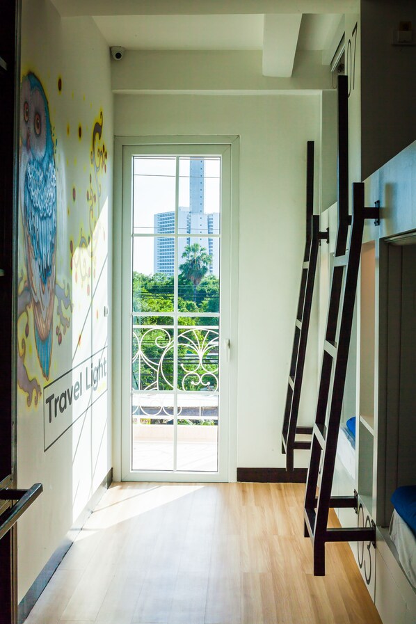 A hotel room with a large window, a balcony with a metal railing, and a wall with a colorful mural.