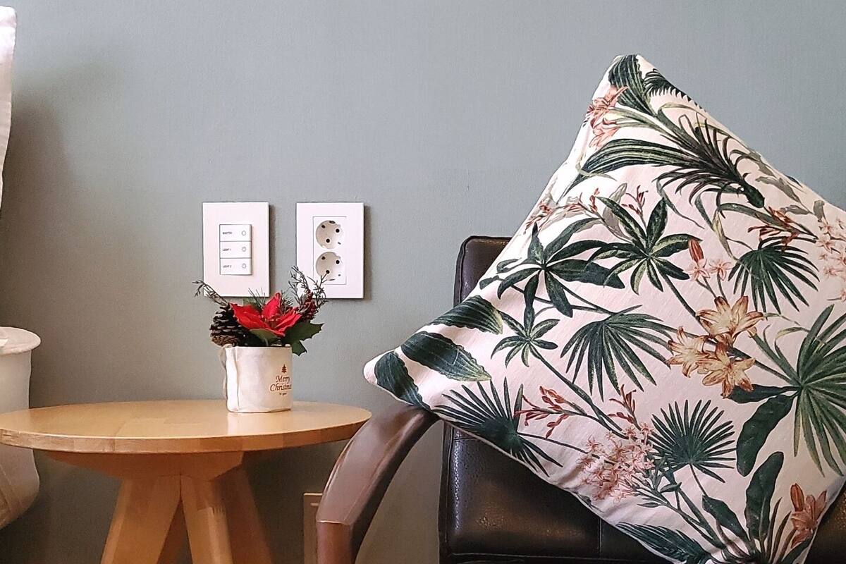 Une pièce avec une table en bois, une chaise agrémentée d’un coussin à motifs floraux et une prise électrique au mur.