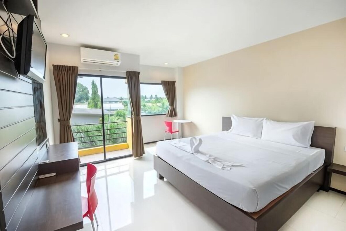 A hotel room with a large bed, a desk, a chair, and a balcony with curtains.