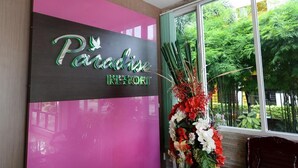 Een receptiegedeelte met een bord waarop 'Paradise Resort' staat en een groot raam met uitzicht op groen.