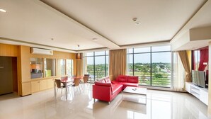 Een moderne woonkamer met een rode bank, een eethoek met stoelen, een televisie en grote ramen met uitzicht op groen.