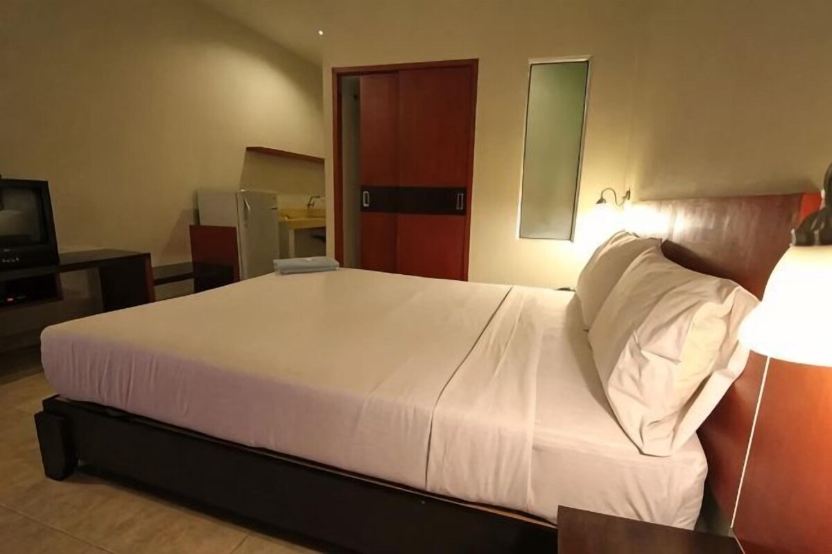 A hotel room with a large bed, a desk with a chair, a television, a wardrobe, and a mirror.