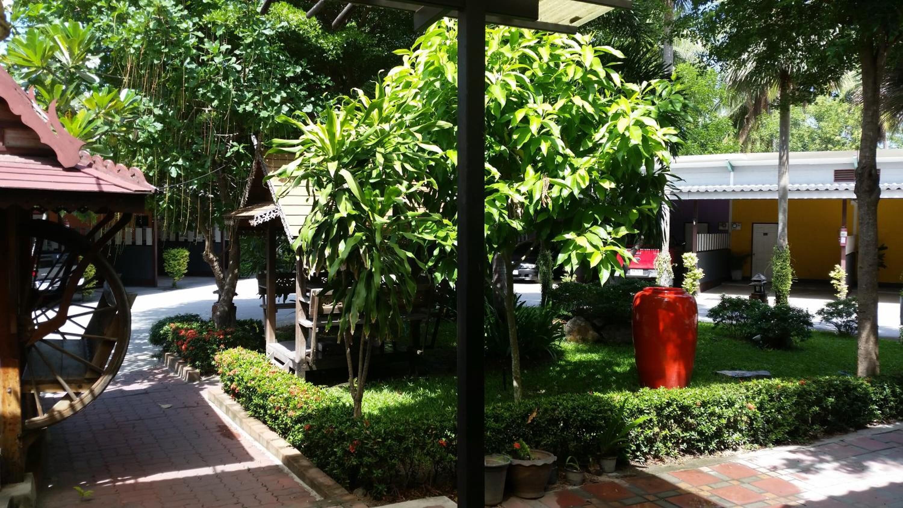 A covered outdoor area with a wooden structure, potted plants, and a red trash bin.