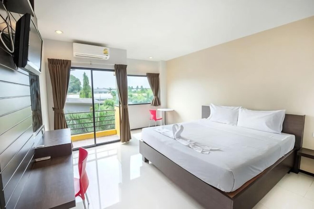 A hotel room with a large bed, a desk, a chair, and a balcony with curtains.