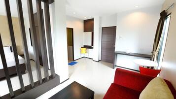 Een moderne hotelkamer met een rode bank, een kleine tafel en een keuken in de achtergrond.