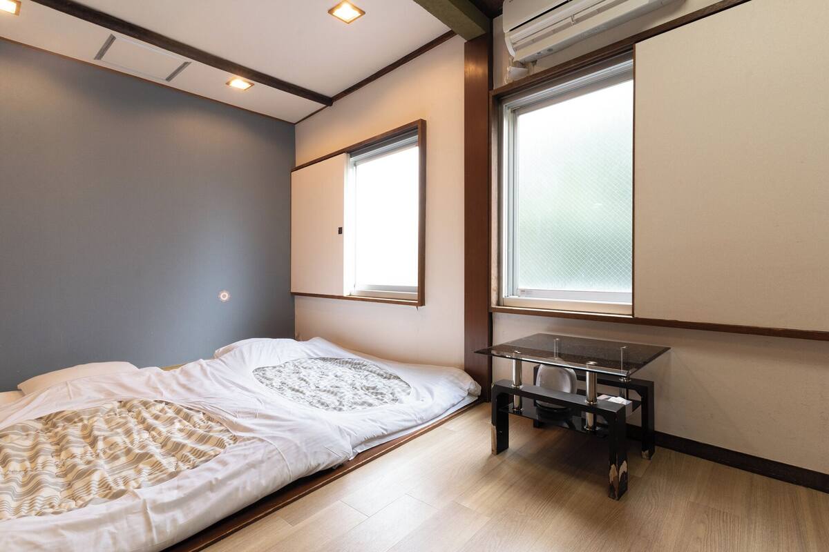 Un dormitorio con una cama, una mesita y dos ventanas.
