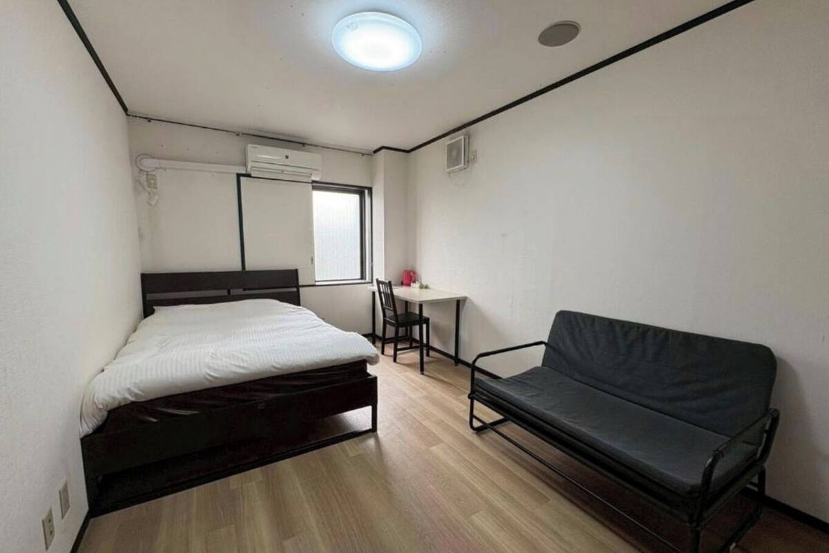Una habitación con cama, escritorio, silla, sofá y aire acondicionado.