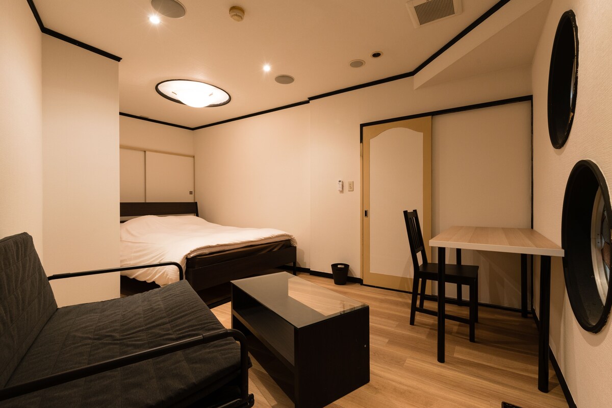 A compact room with a bed, a small table, a chair, and a washing machine.
