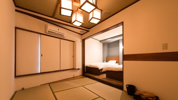 Habitación de hotel con suelo de esteras tatami, una cama con cabecera de madera, un espejo grande y un equipo de aire acondicionado.