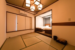 Une chambre d’hôtel avec un sol recouvert de tatamis, un lit doté d’une tête de lit en bois, un grand miroir et un appareil de climatisation.