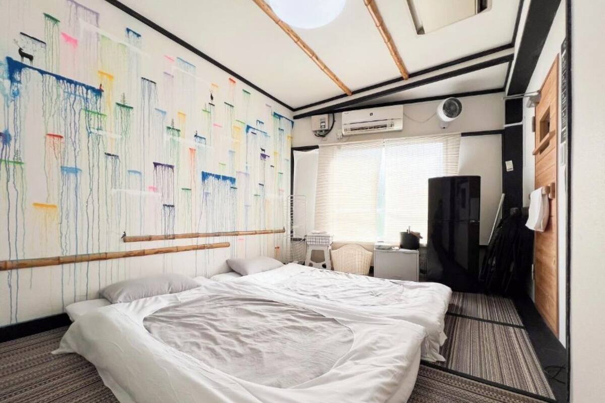 Habitación de hotel con cama, escritorio, silla, unidad de aire acondicionado y ventana con persianas.