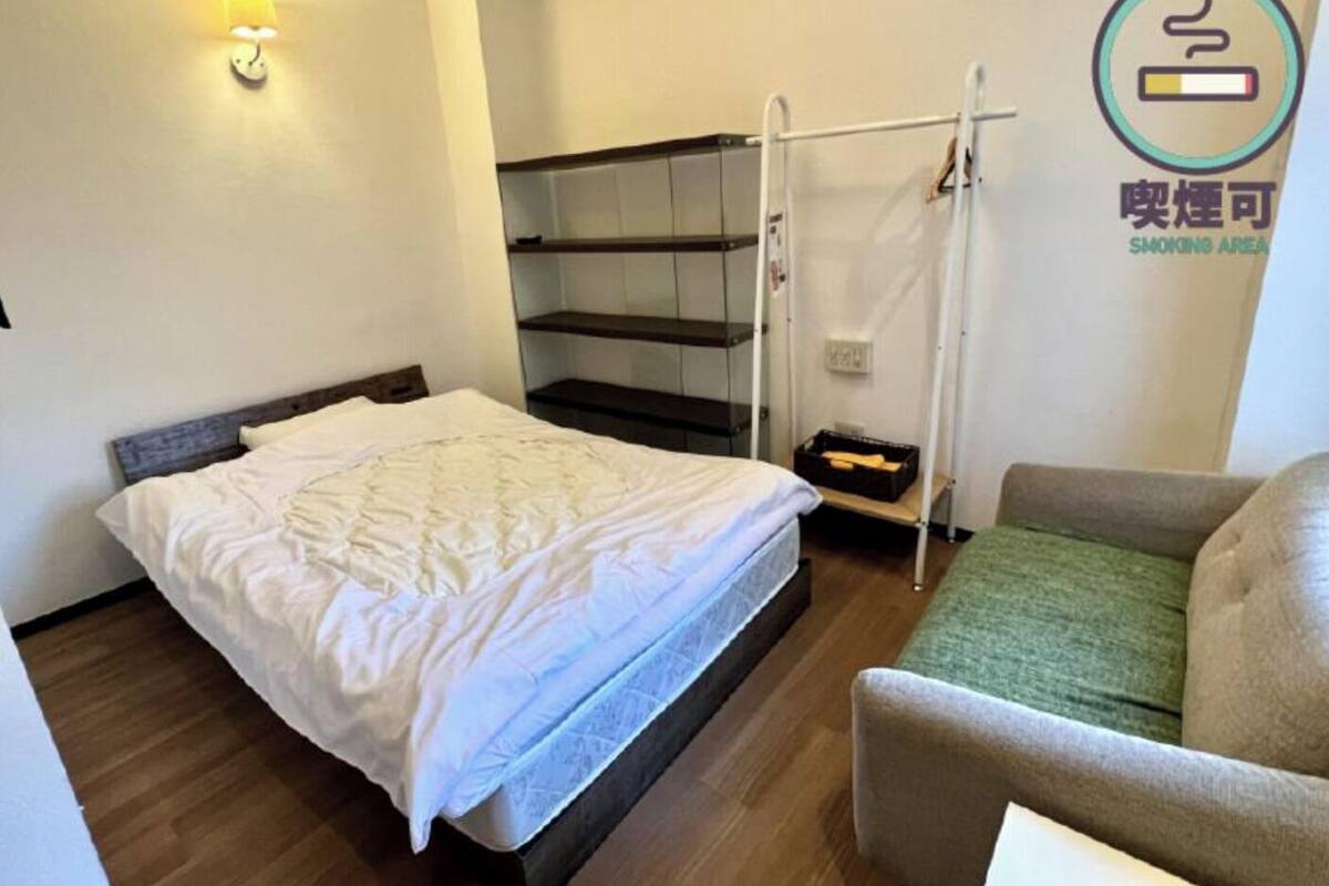 Habitación de hotel con cama, una silla, estante, lámpara de pared y señal de zona para fumadores.