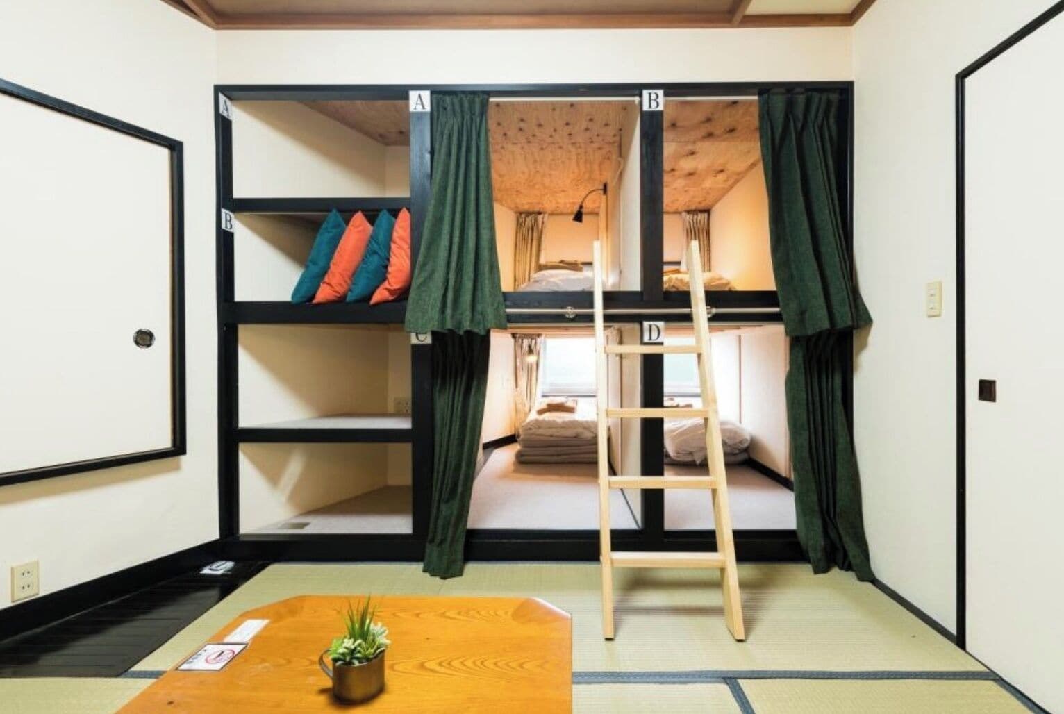 Una habitación con literas, una escalera, una mesita con una planta y suelo de tatami.