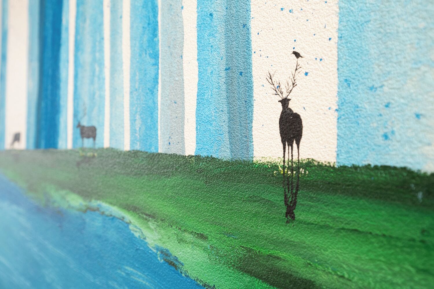 Une fresque représentant un cerf debout dans l’herbe, un oiseau dans le ciel et une vache au fond.