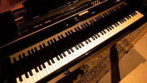 Un piano de cola en una habitación con mesas y sillas, lo que sugiere un comedor o sala de estar.